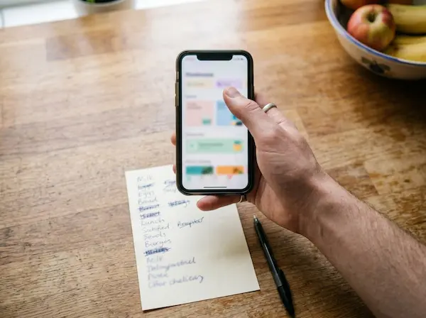 Phone with a budgeting app next to a handwritten grocery list